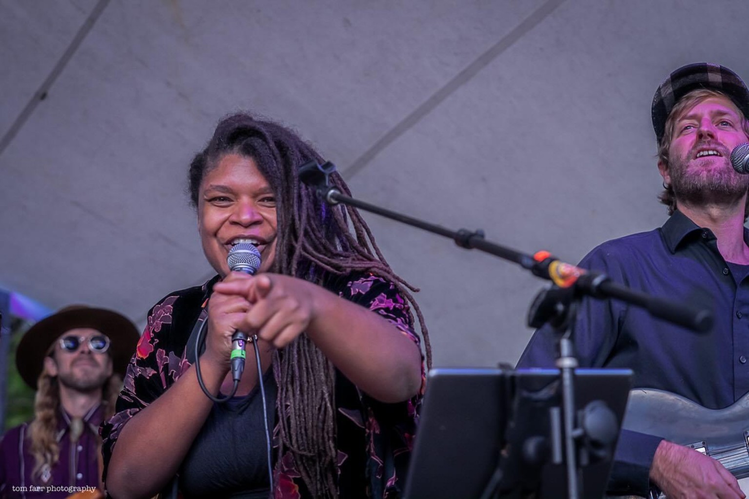Debrissa smiling into a microphone and pointing toward the camera while performing with other musicians